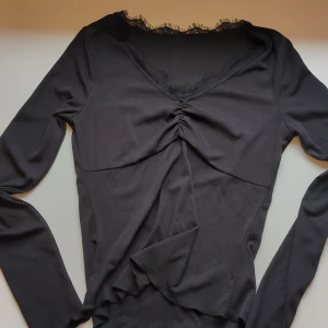 Svart ribbad topp med spets  - Svart långärmad topp med ribbad struktur och snygg v-ringning dekorerad med spetsdetaljer. Toppen har rynkning framtill och är figurnära med mjukt stretchigt material. Perfekt för dig som gillar stilrena och trendiga plagg. Står S men passar nog både S och XS.                                                              Inga bilder på, pga för lite för mig<3 