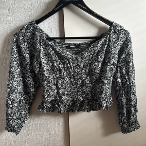 Blommig croppad blus från Bik Bok - Supersöt svartvit blommig blus från Bik Bok med croppad passform och volangkant nertill. Långa ärmar med resår vid handlederna och lätt rynk framtill. Perfekt för dig som gillar romantiska och trendiga detaljer.