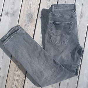 Grå jeans från Jack & Jones - Snygga grå jeans från Jack & Jones i rak modell. Klassisk femficksdesign med bälteshällor och knappgylf. Jeansen har en cool tvättad look och är tillverkade i mjukt bomullsmaterial som är skönt att bära hela dagen. Modellen är regular clark. Det är bara att höra av er vid minsta fråga eller fundering. 