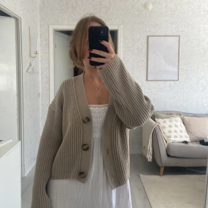 Beige ribbad kofta från H&M - Säljer en beige ribbstickad kofta från H&M med stora knappar framtill. Koftan har en loose passform, v-ringad hals och långa ärmar. Perfekt att slänga över en klänning eller t-shirt för en chill look. Supermjuk och skön att bära.