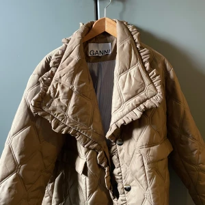 Quiltad beige jacka från Ganni - Säljer en quiltad beige jacka från Ganni med volangdetaljer längs kragen och knäppningen. Har bara använts ca 2 gånger så i väldigt fint skick