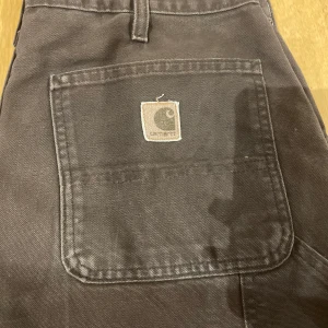 Bruna cargopants från Carhartt - Säljer ett par bruna cargopants från Carhartt med raka ben och flera stora fickor, inklusive två bakfickor med logopatch. Byxorna är tillverkade i slitstark bomull och har en klassisk, loose passform. Perfekta för en streetwear-look. Midjemått är 42cm raktöver 