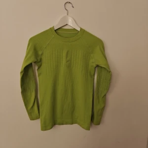 Crivit underställ - Limegrön långärmad tröja från Crivit Sports med coola ribbade detaljer på axlar och ärmar. Tillverkad i en mix av polyamid, polyester och elastan som ger en stretchig och sportig känsla. Perfekt för dig som gillar att sticka ut med färg.