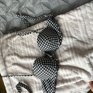 Svartvit rutig bikiniöverdel med volang - Supersöt bikiniöverdel i svartvitt rutigt mönster med volangdetaljer längs kanterna. Bikinin har vadderade kupor och knytband både i nacken och runt ryggen. Perfekt för sommaren och strandhäng!