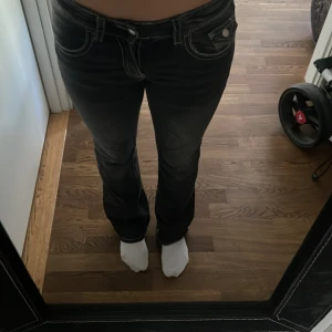 Svarta bootcut jeans Gina Tricot 164 - Snygga svarta jeans från Gina Tricot i storlek 164. Modellen har bootcut-ben, markerade vita sömmar och coola fickdetaljer med lock och knapp. Jeansen har låg midja och är tillverkade i klassiskt denimtyg.