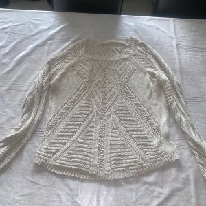 Vit stickad långärmad tröja - Snygg vit stickad tröja med lång ärm och coolt mönster i stickningen. Tröjan har rund hals och ribbade kanter vid ärmslut och nederkant. Perfekt för dig som gillar detaljer och vill ha en mysig men stilren look.