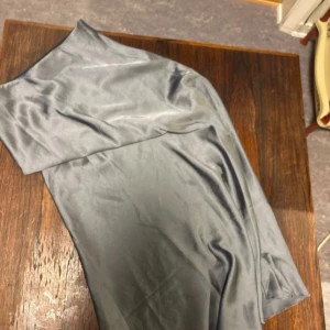 Grå långkjol i satin XS - Snygg grå långkjol från The Black Label Collection i storlek XS. Kjolen har en slät och glansig satinfinish som ger en lyxig känsla. Perfekt för dig som gillar stilrena och eleganta plagg med lite extra shine.