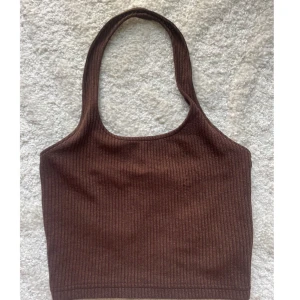 Brun ribbad croppad topp - Lite noppig på ett ställe. Snygg brun croppat linne halterneck och ribbad struktur. Toppen har en enkel, stilren design och är perfekt för att matcha med jeans eller kjol. Materialet känns mjukt och stretchigt, vilket gör den skön att bära hela dagen.