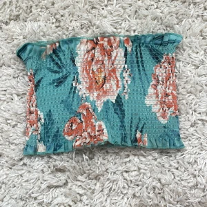 Blommig bandeau tubtopp från Gina Tricot - Superfin bandeau tubtopp från Gina Tricot i turkosblått med stora blommor i orange och vitt. Smockad och elastisk med volangkant upptill och nertill. Perfekt för varma dagar och ger en riktigt somrig vibe.använd mycket utomlands och varma sommardagar perfekt till stranden då kan kanske vill ha lite lätta kläder!💐🩷🥰
