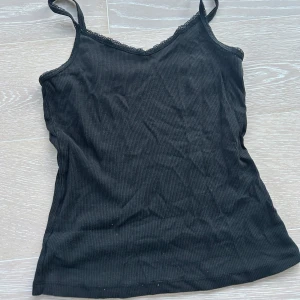 Svart ribbad linnetopp med spets - Svart ribbad linnetopp med smala axelband och v-ringning dekorerad spettslkant i st xxs💕💕
