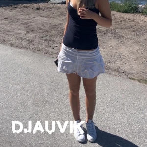 Vit volangkjol med snörning - Supersöt vit kortkjol med volanger och snörning i midjan. Kjolen har en luftig och lätt känsla, perfekt för varma dagar. Sitter snyggt på höften och ger en trendig look. M men passar mer mot s. Går att knyta hur hårt som helst så kan ha som löst och lite fastare.