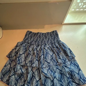 Blå mönstrad volangkjol - Supersöt kortkjol i blå med mönster på. Det finns undershorts i dom. Aldrig använd så är i jättebra skick. Står ingen storlek men jag brukar ha M och skulle säga att den passar S-L-Xl då den har super mycket stretch. Pris kan diskuteras❤️