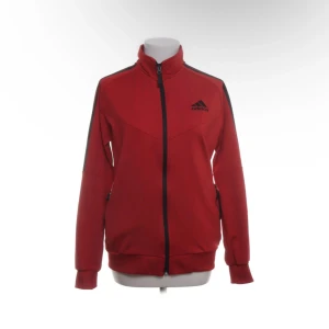 Röd Adidas vindjacka med svarta detaljer - Röd vindjacka från Adidas med svarta ränder längs axlarna och dragkedja framtill. Jackan har hög krage, långa ärmar och två fickor med dragkedja. Perfekt för sportiga dagar och streetstyle. Storlek L, endast testad💖