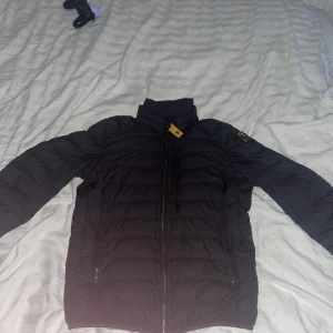Svart dunjacka Parajumpers S - Säljer en svart superlätt dunjacka från Parajumpers i storlek S. Jackan har quiltad design, hög krage och dragkedja framtill. Perfekt för kyliga dagar och har klassisk Parajumpers-logga på ärmen. Snygg och stilren modell som funkar till det mesta.