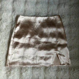 Champagnefärgad kortkjol från Gina Tricot - Säljer en glansig champagnefärgad kortkjol från Gina Tricot i storlek 34. Kjolen har en snygg slits framtill och stängs med dragkedja bak. Tunt, skimrande material som ger en lyxig känsla. Passformen är normal och kjolen är rak i modellen. Några få noppor, annars i bra skick.