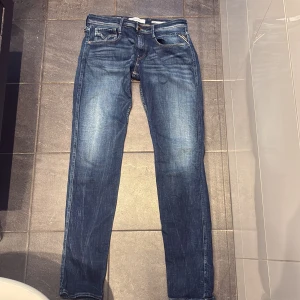 Replay Anbass slim jeans blå - Snygga blå Replay Anbass jeans med slim fit och nästintill aldrig använda. Jeansen har ljusa slitningar framtill, kontrastsömmar och läderpatch bak i midjan. Tillverkade i mjukt denimtyg som sitter skönt hela dagen. Tveka inte att höra av er vid funderingar👌👌