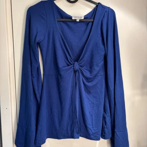Blå långärmad knytblus Design by Si - Supersnygg blå långärmad blus från Design by Si med knyt framtill och djup v-ringning. Toppens material är mjukt och stretchigt, perfekt att styla över ett linne eller topp💛💛