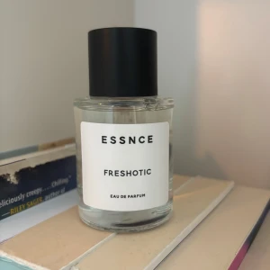 ESSNCE Freshotic Eau de Parfum - Minimalistisk parfymflaska från ESSNCE med doften Freshotic. Flaskan är cylindrisk i genomskinligt glas med en svart, matt kork och vit etikett med svart text. Perfekt för dig som gillar stilren design och fräscha dofter. Använd något sprut 
