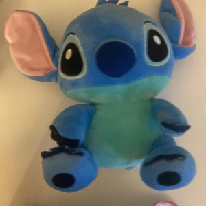Stitch gosedjur  - Bilderna visar en blå plyschleksak som liknar karaktären Stitch från Disney-filmen 'Lilo & Stitch'. Det är en mjuk och färgglad figur med stora öron och ögon, perfekt som present eller dekoration för fans av Lilo och Stitch. jag står inte för om paketet försvinner i frakten. 70 kr plus frakt