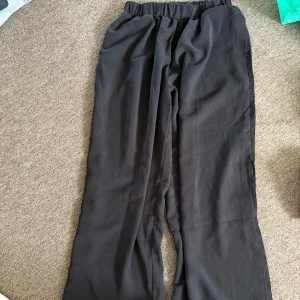 Svarta vida byxor med resårmidja - Säljer ett par svarta byxor med breda ben och skön resår i midjan. De är tillverkade i ett mjukt och lätt tyg som faller snyggt. Perfekta för en chill och avslappnad stil. Passar dig som gillar loose fit och enkel design.