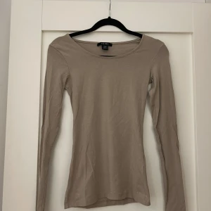 Beige långärmad topp från Amisu - Snygg beige långärmad topp från Amisu i storlek XS. Modellen är slim och har en rundad halsringning. Tillverkad i mjuk bomull som är skön mot huden. Perfekt att styla med jeans eller kjol för en clean och enkel look. Köptes för ett år sedan men enbart använd en gång. Passar även för en S då materialet är mycket stretchigt. 