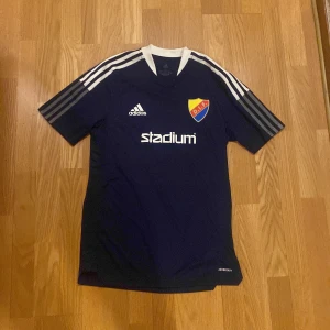 Djurgården fotbollströja Adidas S - Djurgården fotbollströja från Adidas i marinblått med vita detaljer och klassiska ränder på axlarna. DIF-emblem på bröstet, Stadium-logga och Adidas-märke. Tillverkad i Primegreen-material som är lätt och andas. Perfekt för match eller träning. 