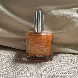 CAIA The Glow Oil Shimmerolja - Säljer CAIA The Glow Oil, en skimrande kroppsolja med guldig ton. Oljan innehåller avokadoolja och vitamin E för extra glow. Kommer i en fyrkantig glasflaska med silvrig kork. Perfekt för att boosta lystern på huden och ge en snygg, solkysst finish. Helt oanvänd!!