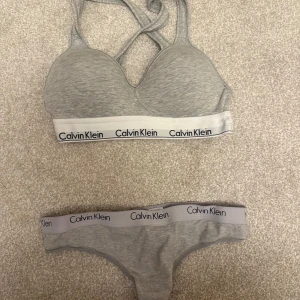 Grå Calvin Klein  - Grått underklädes set från Calvin Klein med klassisk logoresår under bysten. Toppen har vadderade kupor och korsade axelband i ryggen. Mjuk och stretchig bomullsblandning som ger en sportig vibe. Perfekt för en chill och avslappnad look. 449 för båda 