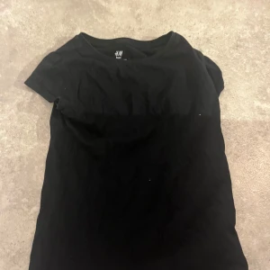 Svart basic t-shirt från H&M - En svart, enkel t-shirt från H&M Basic i ekologisk bomull. Modellen är klassisk med rund hals och korta ärmar, perfekt för en chill och clean look. Passformen är normal och materialet är mjukt och skönt mot huden.