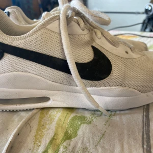 Vita Nike sneakers med svart swoosh - Snygga vita Nike sneakers med svart swoosh på sidorna och vit sula med synlig luftbubbla. Ovandelen är i mesh för extra andningsförmåga och skorna har klassisk snörning. Perfekta för dig som gillar sportig och clean stil.