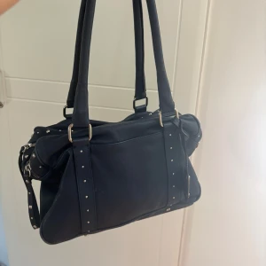 Vintage handväska med nitar  - Cool mörkblå handväska i skinnimitation från  med silverfärgade nitar och detaljer. Väskan har dubbla handtag, flera dragkedjor och metallringar på sidorna. Perfekt storlek för att få plats med allt du behöver och ger en edgy vibe till din outfit.