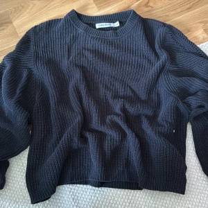 Svart stickad tröja Carin Wester - Mysig svart stickad tröja från Gina Tricot med rund halsringning och ribbad struktur. Tröjan har långärmade ärmar och en relaxed passform som passar perfekt till jeans eller kjol. Enkel och stilren design som funkar året runt.