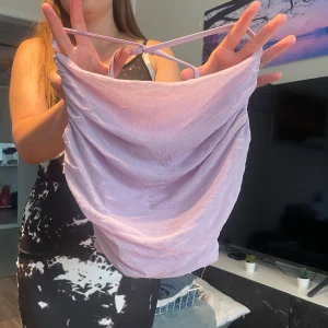 Ljuslila linnetopp med tunna band - Supersöt ljuslila linnetopp med tunna axelband som korsas i ryggen. Toppen har en draperad front och är tillverkad i ett tunt, lätt material som känns svalt mot huden. Perfekt för varma dagar eller när du vill ha en chill och trendig look.