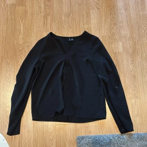 Svart v-ringad blus från Vero Moda - Snygg svart blus från Vero Moda i storlek XS. Blusen har en v-ringad hals och långa ärmar med knappdetalj. Materialet är mjukt och lätt, perfekt för dig som gillar stilrena och enkla plagg. Passar till många olika outfits och är enkel att matcha.