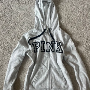 Grå hoodie från PINK Victoria's Secret - Grå hoodie med dragkedja från PINK Victoria's Secret. Köpt för flera år sedan, och säljer då jag inte använder den. Använd några gånger men ser helt ny ut. Skriv om ni har några frågor!🩷