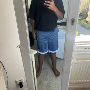 Blå loose shorts från SHEIN - Snygga blå shorts från SHEIN med vit kant längst ner. Modellen är loose fit med elastisk midja och två stora fickor framtill. Perfekta för chill dagar och har en cool street vibe. Materialet känns lätt och skönt mot huden.
