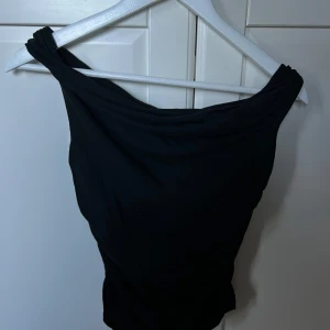 Svart one shoulder topp - Säljer en svart one shoulder topp med twistad axel. Toppen är tunnare och mjuk i materialet, stretchig och bekväm. Passar asbra till ett par jeans eller en kjol!!!☺️