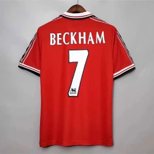 Manchester United Beckham 7 tröja - Klassisk röd Manchester United fotbollströja med BECKHAM och nummer 7 på ryggen. Tröjan har korta ärmar, vita och svarta detaljer på krage och ärmslut samt svarta ränder på axlarna. Perfekt för dig som älskar fotboll och retrostil.
