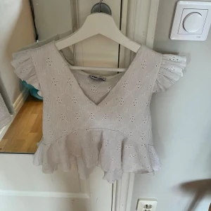 Vit blus med volang från FB Sister - Supersöt vit blus från FB Sister med broderade hål och volang nertill. Toppen har v-ringning, korta volangärmar och är gjord i bomull. Kommer tyvärr inte längre till användning. Även fast den är i storlek M så passar den mig perfekt som vanligtvis har storlek Xs/S. 