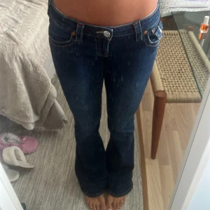 True Religion Joey Low Rise Flare Jeans - Säljer ett par mörkblå True Religion Joey jeans med låg midja och flare-ben byxan ÄR UPPSYDD då den var för lång förut. Klassiska kontrastsömmar, snygga fickdetaljer med knappar bak och ikonisk True Religion-lapp. Jeansen är i stretchig denim och har en riktigt schysst passform. Säljer på grund av att jag hade behövt en storlek mindre.