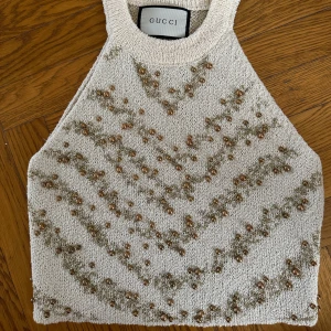 Gucci stickad topp - Exklusiv stickad linnetopp från Gucci i beige med guldiga pärlor och glittriga detaljer i chevronmönster. aldrig använd. Toppen är halterneck och har en lyxig känsla tack vare pärlorna och det glittriga garnet. Perfekt för dig som vill sticka ut med något unikt.