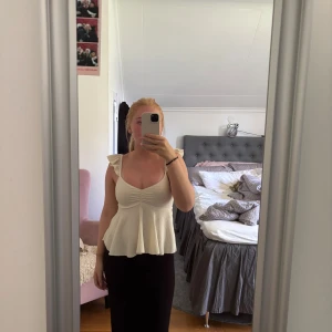 Vit linnetopp med volangaxelband - Supersöt vit linnetopp med volangprydda axelband och lätt rynk framtill. Utsvängd nertill för en flowy känsla och djup urringning. Perfekt för varma dagar och ger en romantisk vibe till outfiten.