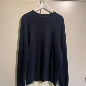 J.lindberg sweatshirt mörkblå - Snygg mörkblå sweatshirt från J.Lindeberg i klassisk modell med rund hals och diskret logga på bröstet. Tröjan är tillverkad i mjuk bomull och har långa ärmar samt ribbade muddar vid ärmslut och nederkant. Perfekt för en clean och stilren look. Storleken är size M men väldigt stor för storlek medium. Nypris 1600kr köpt för ca 4 månader sedan. Mått: Axel-Axel ca 70cm, Mått Axel-midja ca 70cm. Från krage-vrist: ca 90cm. Bredd mage ca 57cm