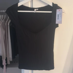 Svart topp med v-ringning från Nelly - Svart topp från Nelly med v-ringningr. Toppen har en smal passform och diskret spetskant längs halsringningen som ger en söt detalj. Helt oanvänd med lapp kvar