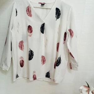 Vit blus med fjädermönster - Vit blus från Zara med v-ringning och trekvartsärm. Blusen har ett snyggt fjädermönster i vinrött och svart som ger en cool och trendig vibe. Lätt och flowigt material som känns skönt mot huden.