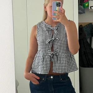 Svartvit rutig blus med rosetter - Säljer en söt blus i svartvitt rutigt mönster med tre knytrosetter framtill. 