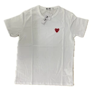 Comme des Garçons T-shirt - Vit t-shirt från Comme des Garçons Play med det ikoniska röda hjärtat broderat på bröstet. Klassisk passform med rund hals och korta ärmar. Perfekt för en clean och stilren look.