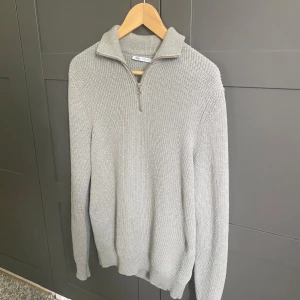 Grå stickad half zip-tröja från Zara - Säljer en grå stickad tröja från Zara med half zip-dragkedja och hög krage. Tröjan är långärmad och har en chunky stickad struktur som ger en snygg och avslappnad vibe. Perfekt för lager-på-lager under höst och vinter.