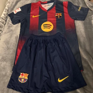 FC Barcelona matchtröja Nike - Säljer en officiell FC Barcelona matchtröja från Nike med tillhörande shorts. Tröjan har klassiska blå och röda vertikala ränder, klubbmärke och sponsorlogga på bröstet samt gula Nike-detaljer. Materialet är lätt och andas, perfekt för fotbollsträning eller match.