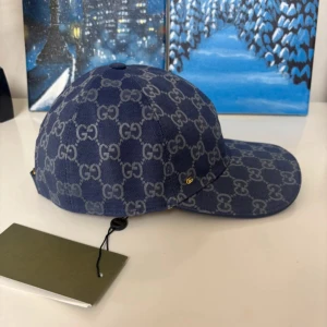 Blå Gucci keps med GG-mönster - Snygg blå keps från Gucci med klassiskt GG-monogram i grått över hela kepsen. Justerbar rem baktill i blått och insida i ljus bomull. Perfekt accessoar för dig som vill sticka ut med lyxig streetstyle.